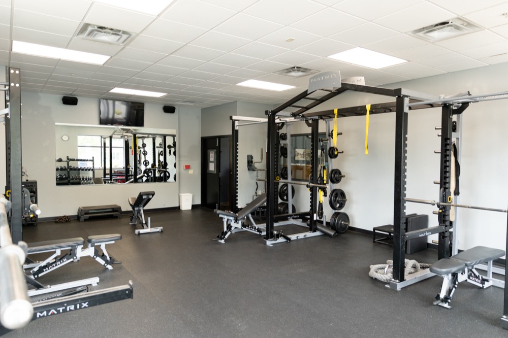 A bright gym with weight racks, benches, mirrors, and various exercise equipment arranged neatly on a black floor.